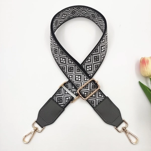 Close-up of geometric jacquard bag strap with grey leather ends and gold metal hooks
