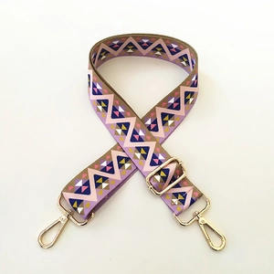 Macro detail of geometric patterned bag strap with golden metal swivel hooks and buckle
