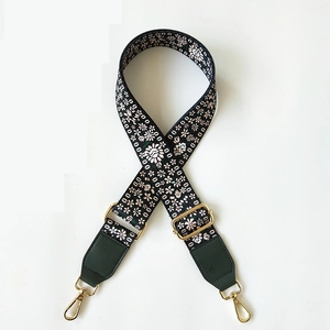 Close-up of vintage floral embroidery on dark green bag strap with gold metal hooks