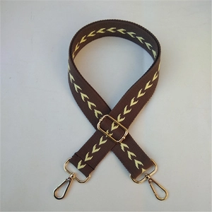 Detail of coffee-colored woven strap with yellow arrow pattern and gold metal buckles