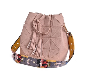 Detail of light pink bucket bag with geometric stitching and colorful woven strap