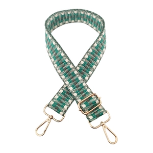 Detail of adjustable woven bag strap with green and white geometric jacquard and gold hooks