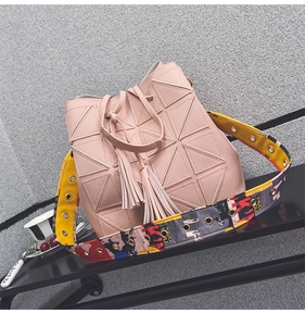 Detail of pink geometric bucket bag with wide floral woven strap and tassel accents