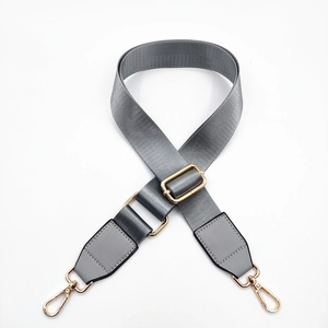 Detail of grey nylon shoulder strap with golden metal buckles and leather trim