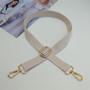Dettaglio di tracolla in tela beige con moschettoni dorati e fibbia regolabile