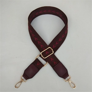 Detail of adjustable woven bag strap with red V-pattern and gold metal swivel hooks