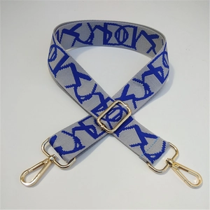 Detail of adjustable woven wide bag strap with grey and blue geometric patterns and gold metal hardware
