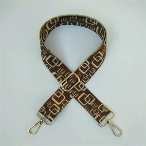 Detail of adjustable geometric bag strap with brown pattern and gold metal hooks