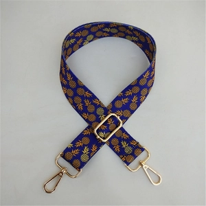 Detail of adjustable wide canvas bag strap with pineapple patterns and golden metal hooks