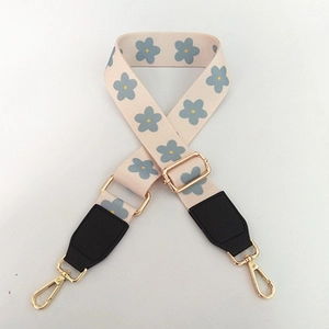 Detail of adjustable woven handbag strap with blue floral pattern and gold metal hooks