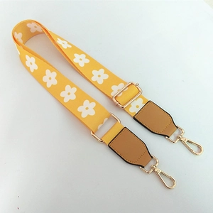 Close-up of adjustable yellow canvas bag strap with white daisy pattern and gold hooks