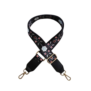 Detail of floral ethnic embroidery on adjustable wide crossbody bag strap with gold hooks