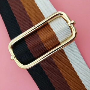 Detail of adjustable striped woven bag strap with premium gold metal hardware buckle