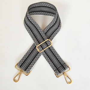 Detail of black and white woven bag strap featuring adjustable golden metal hardware