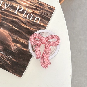 Detailed top view of pink rhinestone bow phone grip holder on a desk with a magazine