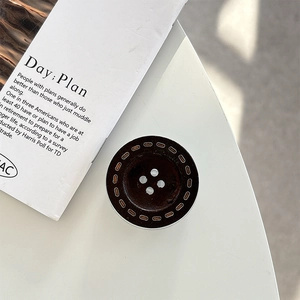 Detail of a dark brown resin button phone grip with stitching on white desk surface