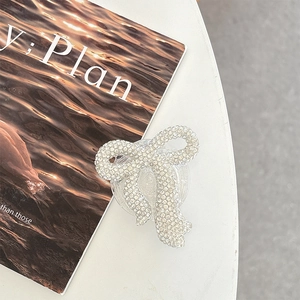 Detail of a sparkling bow-shaped phone grip with pave crystal rhinestones on white desk