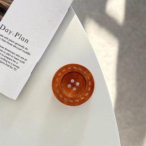 Detail of a brown wood-textured resin button phone stand with four holes and dot pattern