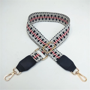 Detail of adjustable woven bag strap with red and black geometric patterns and gold metal clips