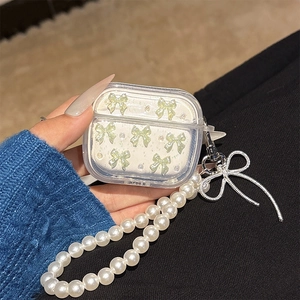 Detail van transparante AirPods hoes met crème groene strikken en parelketting