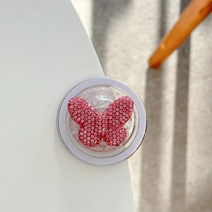 Close-up of pink rhinestone butterfly phone grip with glitter finish on white surface