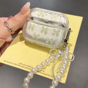 Detail van transparant AirPods-hoesje met groene strik en parelketting op gele kaart