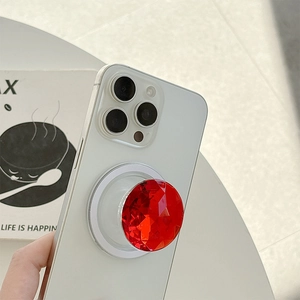 Red rhinestone faceted pop-socket grip attached to a white smartphone back on a desk