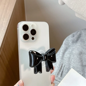Detail shot of a black bow-shaped pop socket phone grip on a white smartphone back