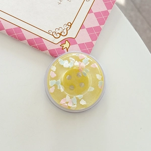 Macro view of a yellow resin phone grip shaped like a button with colorful heart sequins