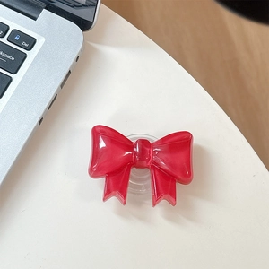 Detail of red bow-shaped expanding phone grip stand on white desk near laptop