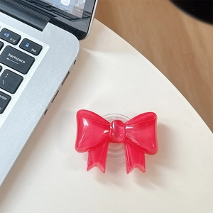 Detail of transparent rose red bowknot phone grip on a white surface next to a laptop
