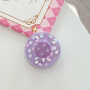 Macro detail of purple button-style phone grip with embossed clouds on white desk