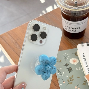 Blue 3D floral phone grip stand with speckled texture on a white smartphone back