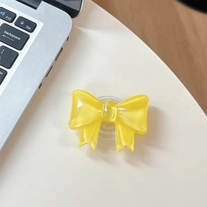 Close-up of a glossy yellow bow phone socket grip on a white desk with a laptop