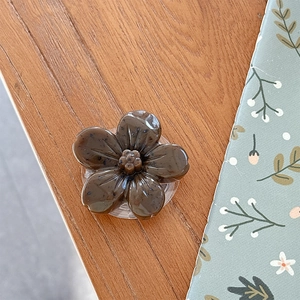 Detail view of a 3D caramel flower phone grip holder on a warm wooden background