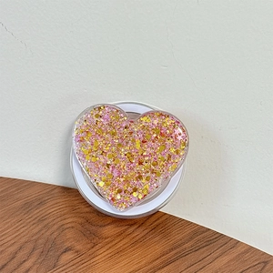 Detail of heart-shaped phone grip with sparkling pink and gold sequins on a wooden desk