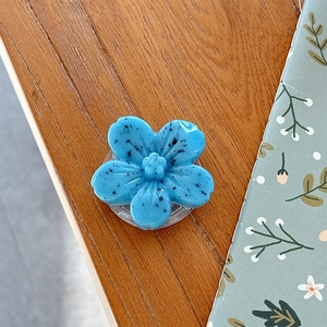 Blue flower phone grip with black ink splatter on warm wooden table for movie viewing