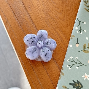 Detailed close-up of light purple floral phone grip with ink splatter pattern on wood