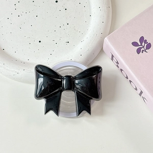 Detail of a black bow-shaped magnetic phone grip with a glossy finish on white dots background