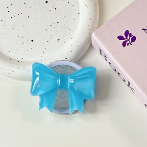 Macro detail of glossy blue bow-shaped MagSafe phone grip on a stylish white base