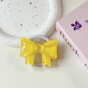 Close-up of yellow resin bow MagSafe phone grip on a white ceramic tray setup