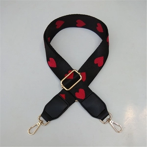 Detail of black fabric bag strap featuring red heart embroidery and golden metal buckles