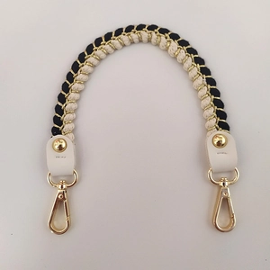 Close-up of hand-woven black and gold bag strap with leather ends and metal lobster clasps