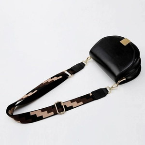 Detail of adjustable geometric jacquard shoulder strap on a black saddle bag with gold hardware