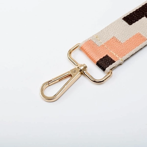 Detail of adjustable woven wide bag strap with geometric patterns and gold metal clasps