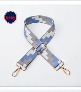 Detail of adjustable woven bag strap with geometric gray pattern and gold metal hooks