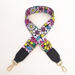 Detail of adjustable woven bag strap with colorful floral pattern and gold metal hooks