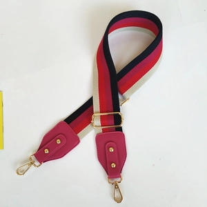 Close-up of a wide colorful striped bag strap with gold metal hooks and pink leather accents