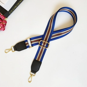 Macro detail of adjustable striped nylon bag strap with gold metal hardware and leather ends