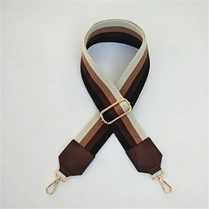 Close-up of adjustable striped canvas bag strap with leather ends and gold metal hooks